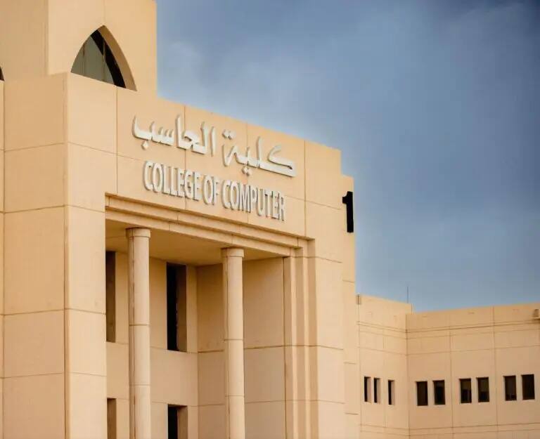 مبنى لون ذا بيج، يتكون من أعمدة ونوافذ مقوسة، تطفوه باللغتين العربية والإنجليزية تحمل اسم "كلية الحاسب" تحت سماء ملبدة الأرنب.