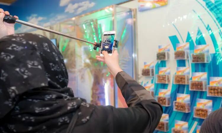 شخص يرتدي غترة سعودية من جاكوزية ويضع عقالاً أنيقاً، يستخدم عصا التصوير الذاتي، وصورة أمام جدار العرض والتعاون العمالي الصغير، يُحتمل أن تكون منتجات تمارس من علامة "النخلة"، وذلك ضمن فعالية لمهرجان الخيال الجنادرية، حيث يسلط الضوء على المكان مقابل زاهية. اكتمل سجل السعودية التراثية بارتداءه البشت السعودي الرسمي المعبر عن الهوية الوطنية.