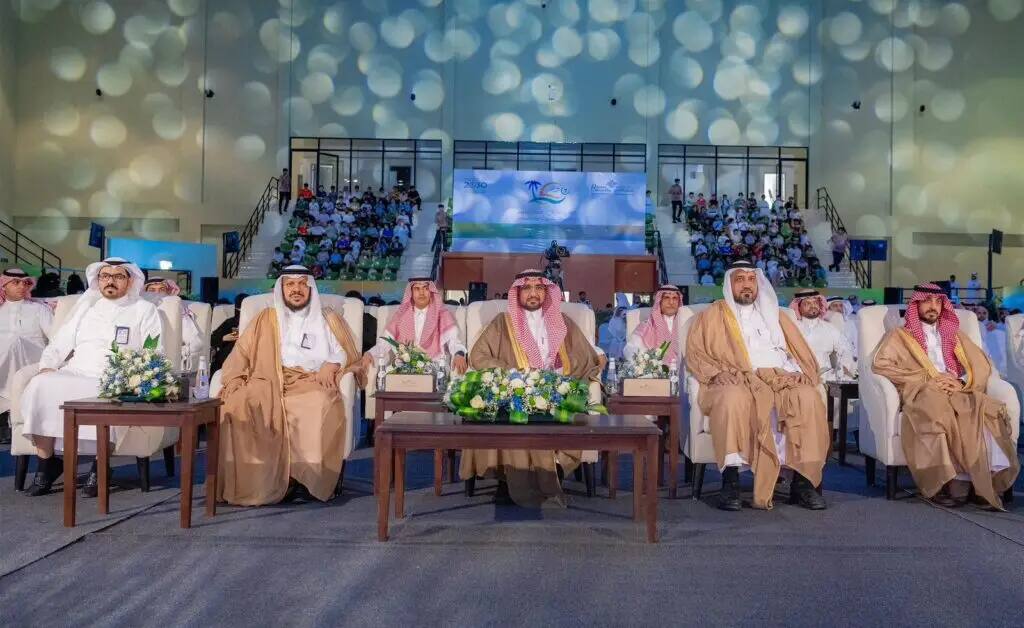 A group of men wearing the Ghattara, or shemagh and aqal, as well as the Saudi bisht, are in the front row of an official event held inside the auditorium at Qassim University as part of the seventh summer club. Flower arrangements adorn the tables in front of them, while in the back a large audience of an estimated 45,000 patrons is visible.