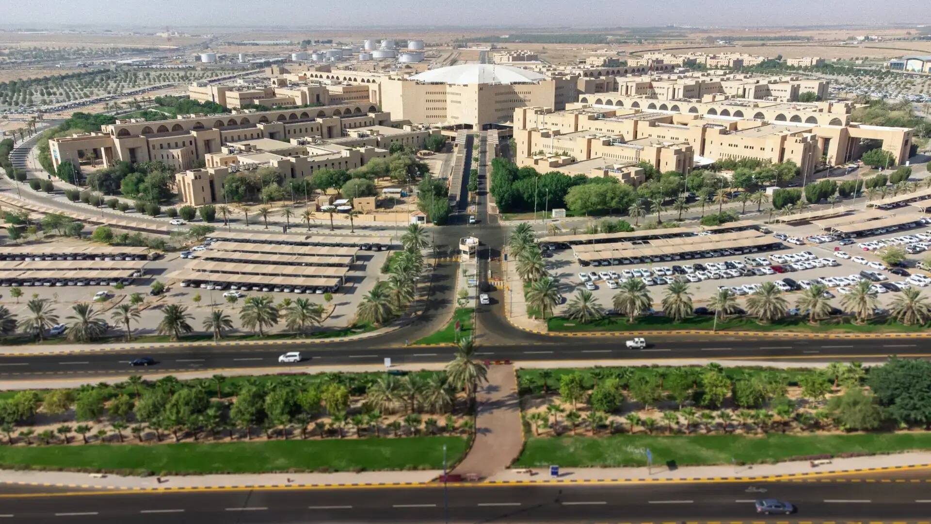 منظر جوي لجامعة القصيم يُظهر الحرم الجامعي الواسع ذو مساحات واسعة ومبانيه المتعددة، ورسومات السيارات وأشجار النخيل والمساحات الخضراء والطرق البحرية. ويمكن رؤية عدد من المشاركين مرتدين الغترة أو الشماغ السعودي مع العقال والبشت السعودي في أي مجتمع ت يعبر عن استدامة الموروث خلال الفعاليات العلمية الدولية بل التي تحتضنها الجامعة.