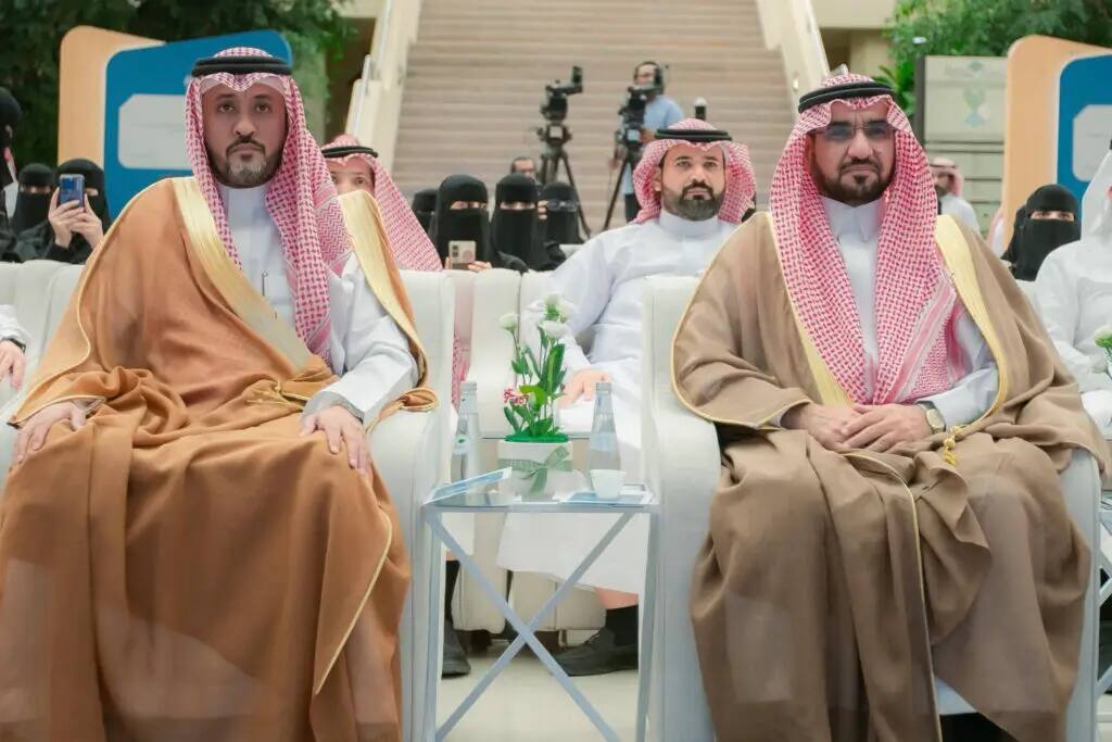 A group of men wearing the Saudi ghutra, shemagh, aqal and Saudi bisht, as well as black women wearing abaya, have become a fixture at Qassim University. They sit in the front row on benches with five flower arrangements in the center, while participants and photographers document the number of people in the crowd.