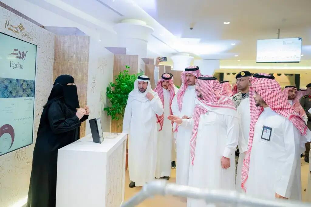 In the university gallery, a group of men wearing a ghutra or shemagh, an aqqal and a Saudi bisht connect with a woman, dressed in a black abaya and niqab, listening intently to a presentation in one of the interior corners. Security men are seen in the background during the event highlighting the Buraydah Dates Carnival.
