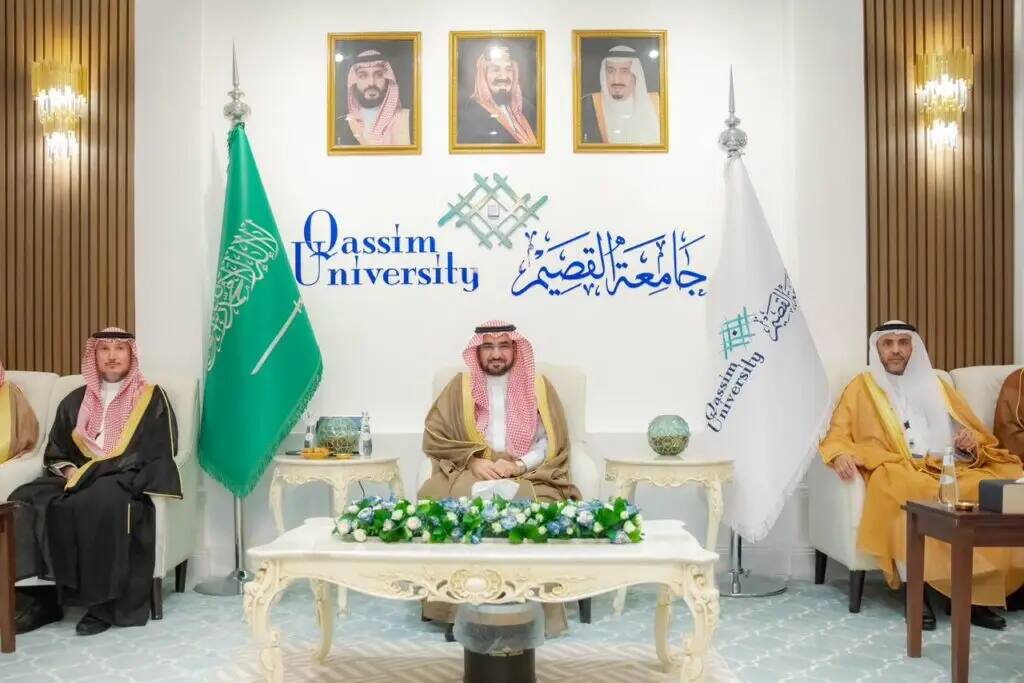 At Qassim University, Saudi officials, wearing the Saudi ghutra or shemagh with an aqal, as well as the Saudi bisht, sit on ornate chairs. Surrounded by the flag of the Kingdom of Saudi Arabia and the University of Manasirin, and topped by portraits of the country's leaders, in a scene that epitomizes Saudi Arabia's prestige and formal traditions.