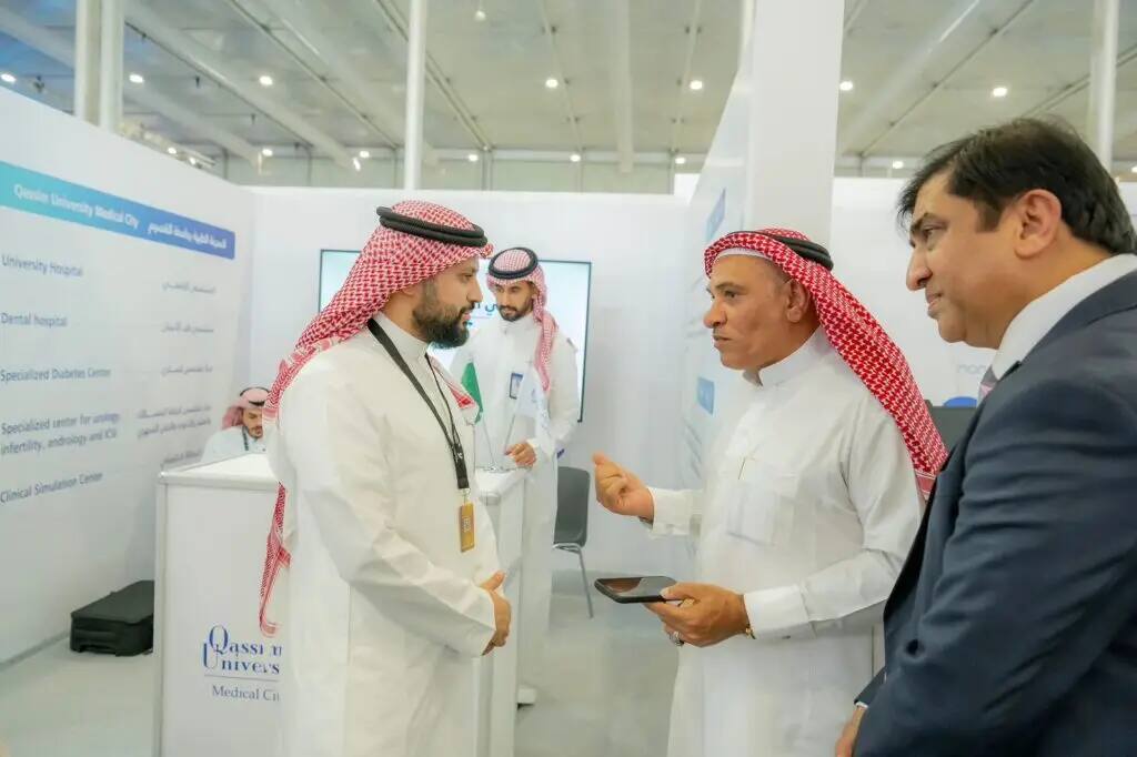 A group of men dressed in Saudi bisht, ghutra and aqal, as well as Nazi shepherd's shirts, exchange experiences about medical studies inside the exhibition's pavilion. One squeezes a tablet while the other naps intently amid the informational screens and information boards of the Qassim University pavilion.