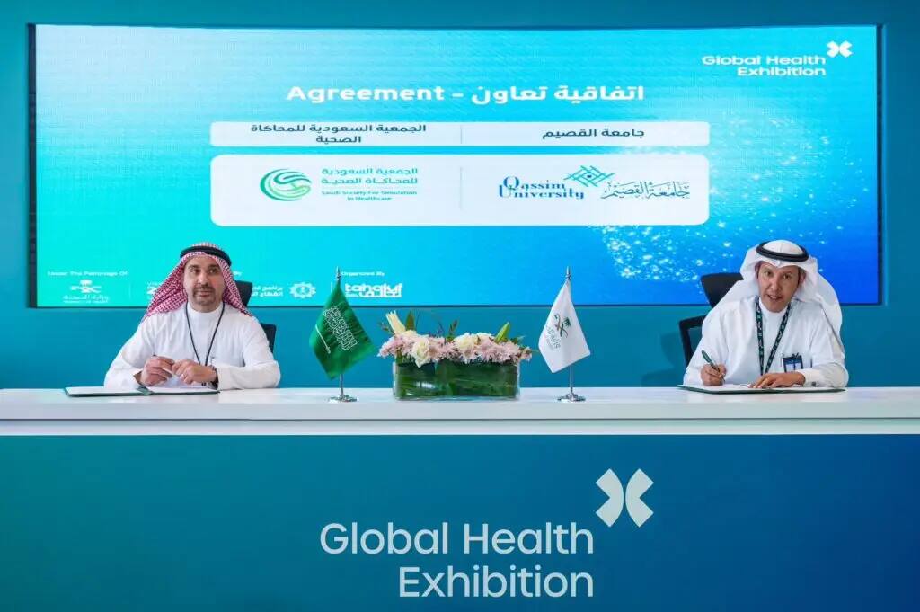 A man dressed in traditional Saudi dress, Saudi shemagh and thobe, at a table at the World Health Expo where he signed a number of documents that represent and symbolize the cooperation between Qassim University and the Saudi Society for Simulation; to dietary supplements and medical expertise.