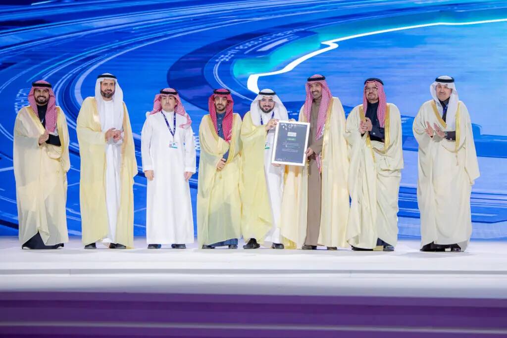 وقف عدد من الرجال مرتدين الشماغ أو الغترة السعودية بالإضافة إلى البدلات الرسمية على منصة الاحتفال، حيث كان الصراع درعاً يتذكرها، وذلك أمام خلفية رقمية زرقاء تتكاملات جامعة القصيم في مجال التحول الرقمي.
