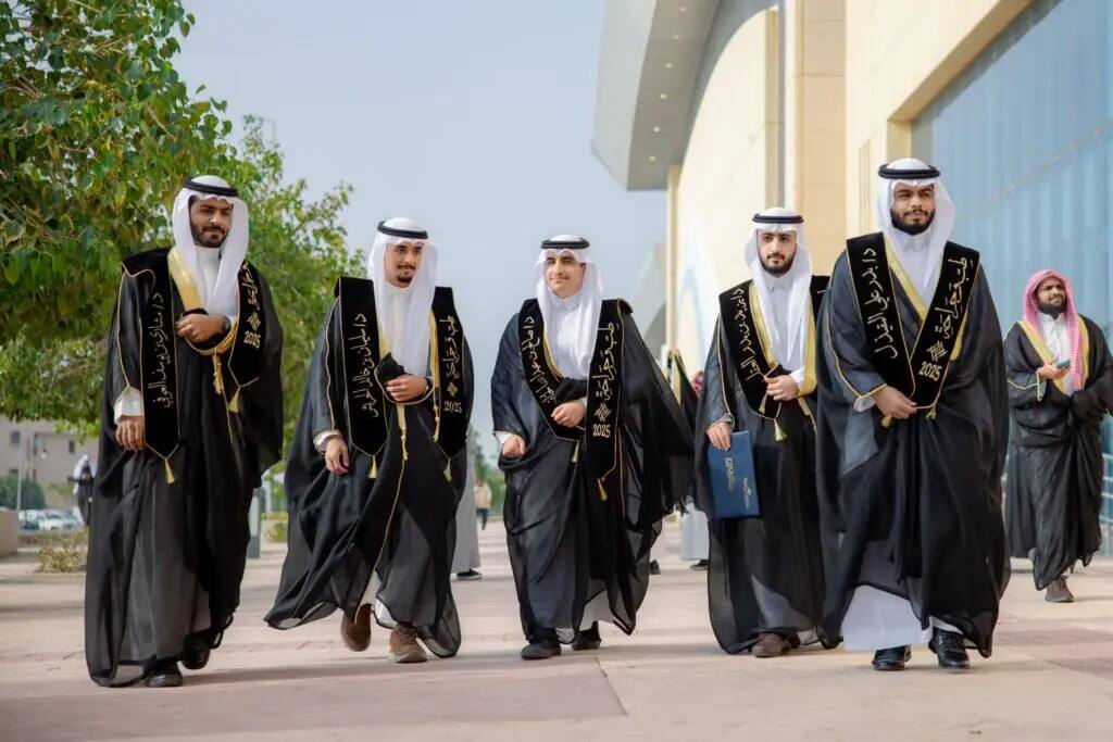 Five men in authentic Saudi garb with a shemagh or Saudi ghutra, plus a liberation maiden, will walk out of a new generation after graduating from university, smiling and relaxed. They are followed by another in costume. They are surrounded by diverse elements in the background of a clear sky.