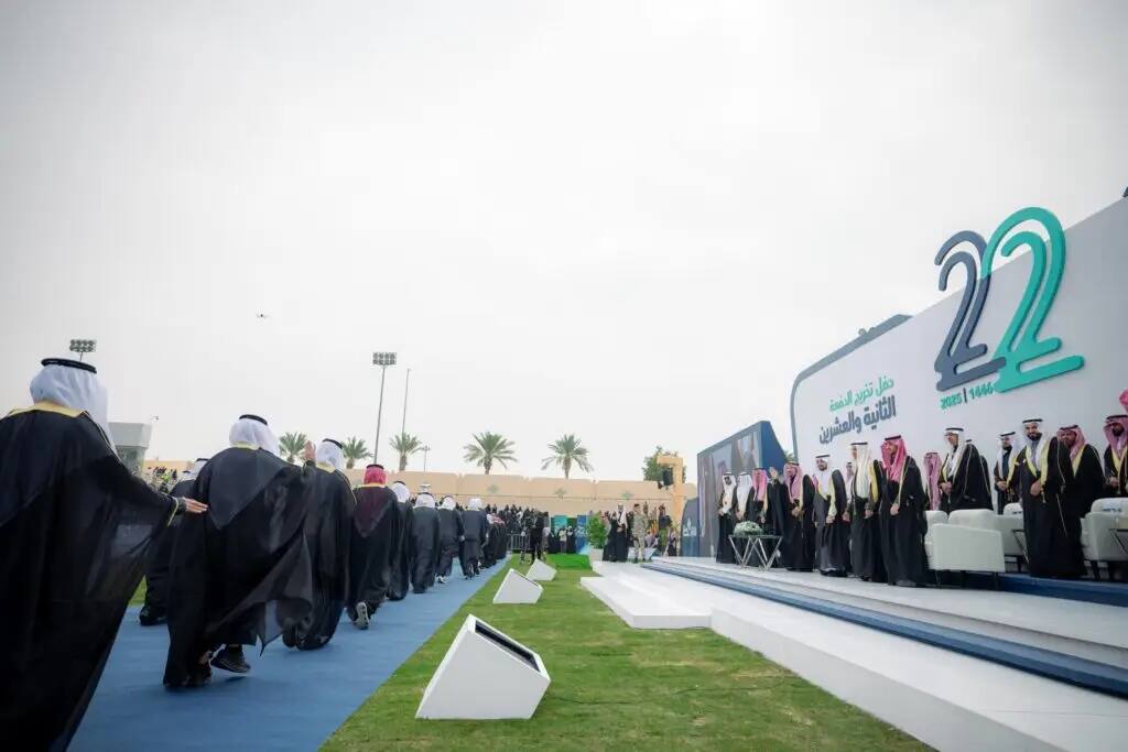 In the open air, attendees will wear Saudi uniforms, including graduates who will walk up to the podium and be seated with officials and the Emir of Qassim. Learn in the background #22 and related Arabic texts in Qassim, palm trees and cloudy skies.
