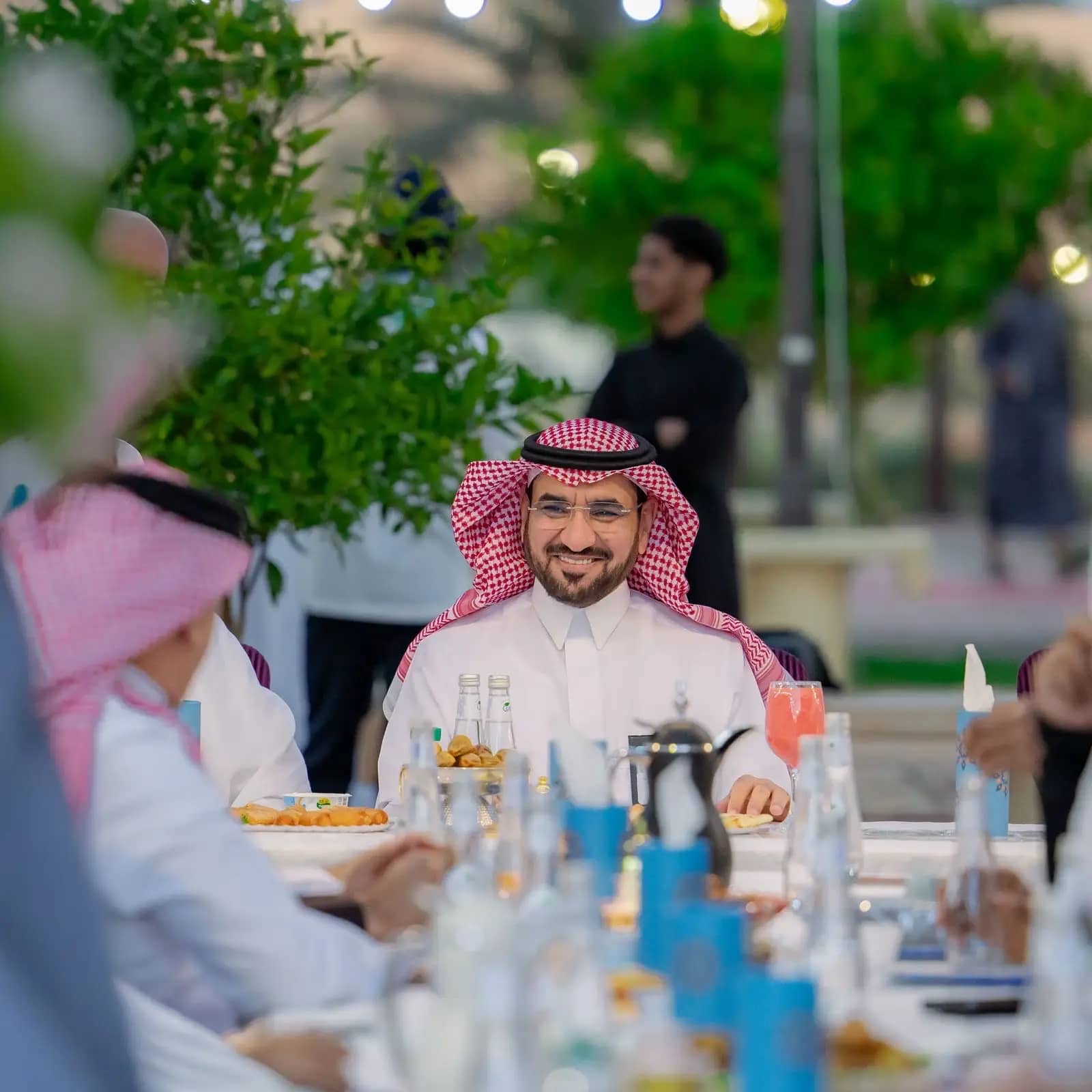 يجلس رجل مبتسم مرتديًا الزي السعودي التقليدي، يشمل الشماغ أو الغترة السعودية، إلى طاولة في الهواء الطلق خلال برنامج الريان الرمضاني، وحوله عدد من الحضور. وتسود لعدم وجود رمضانية مميزة تتخللها واتخاذ الإجراءات المتنوعة، وتضفي حضور رئيس الجامعة بين الضيوف اقرأ من الأهمية والرسمية في اللقاء.