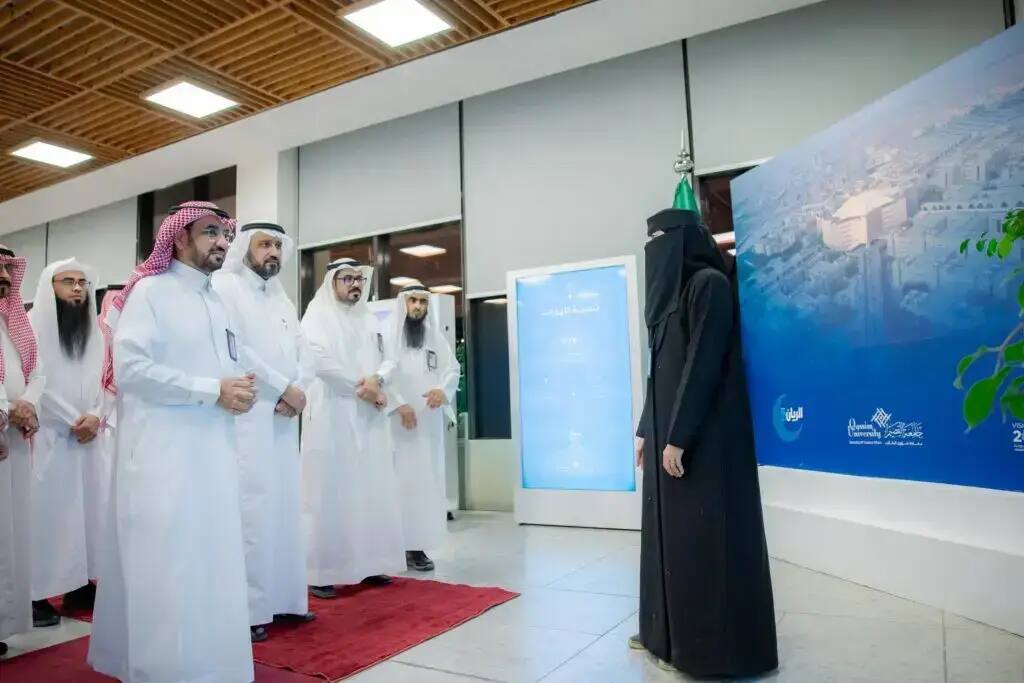A group of men wearing the traditional Saudi shemagh or ghutra, along with a girl dressed in white, come to an enclosed space next to a traditional dressing board with text and images in Arabic. They move on to the Rector's University.