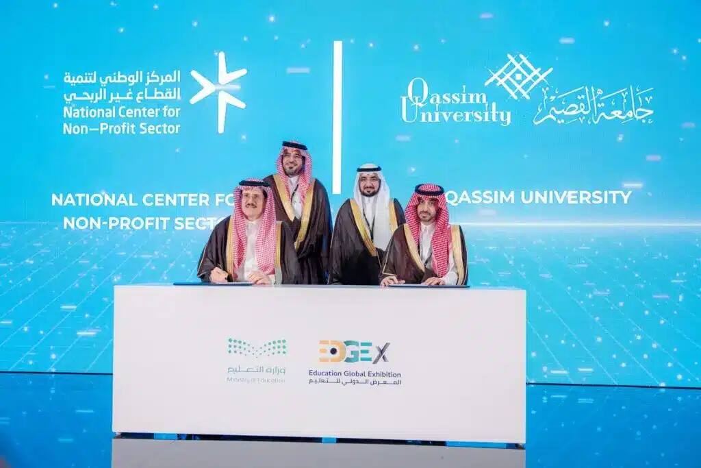 The cat Four men dressed in the Saudi Ghutra or Shemagh, Egal and Pasht sit around a table, smiling casually. They sit behind the logos of the National Center for Investment in the Nonprofit Sector and Qassim University, with the words "Diversified Services for the Nonprofit Sector" highlighted on the blue digital paste.