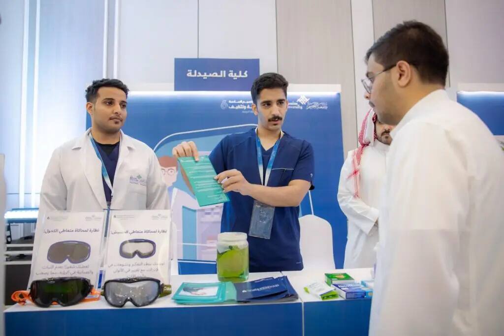كل ثلاثة رجال غترة سعودية، عقال، وبشت سعودي رسمي في جناح كلية الصيدلة في القصيم لغرض تعزيز الصحة والتثقيف. وهو أحد بشرح تعريفي لزائر يهم، بينما تُعرض على طبي خاص وبعض الكتيبات التوعوية ووراء طبية.