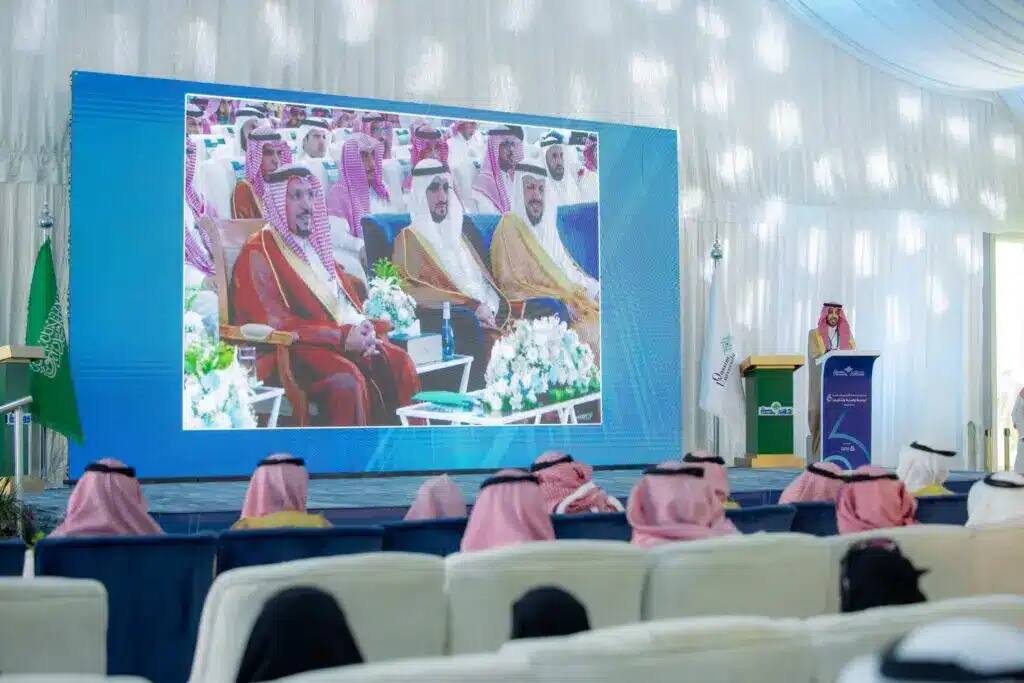 يتحدث واحد فقط من على منصة الخطابة أمام الحضور في خيمة واسعة لحملة الجامعة الشاملة، حيث يظهر خلفه شاشة كبيرة تعرض صورًا لمسؤولين سعوديين وصاحب السمو أمير منطقة القصيم أثناء الحضور المقامة في مقاطعة النبهانية. وظهرت أعلام المملكة العربية السعودية وستائر جزئية كاملة المكان، بينما يبرز عدد من الحضور مرتدين الغترة أو الشماغ مع العقال والبشت السعودي بما في ذلك دقة الهوية الوطنية وروح الشرعية الرسمية لجامعة القصيم.