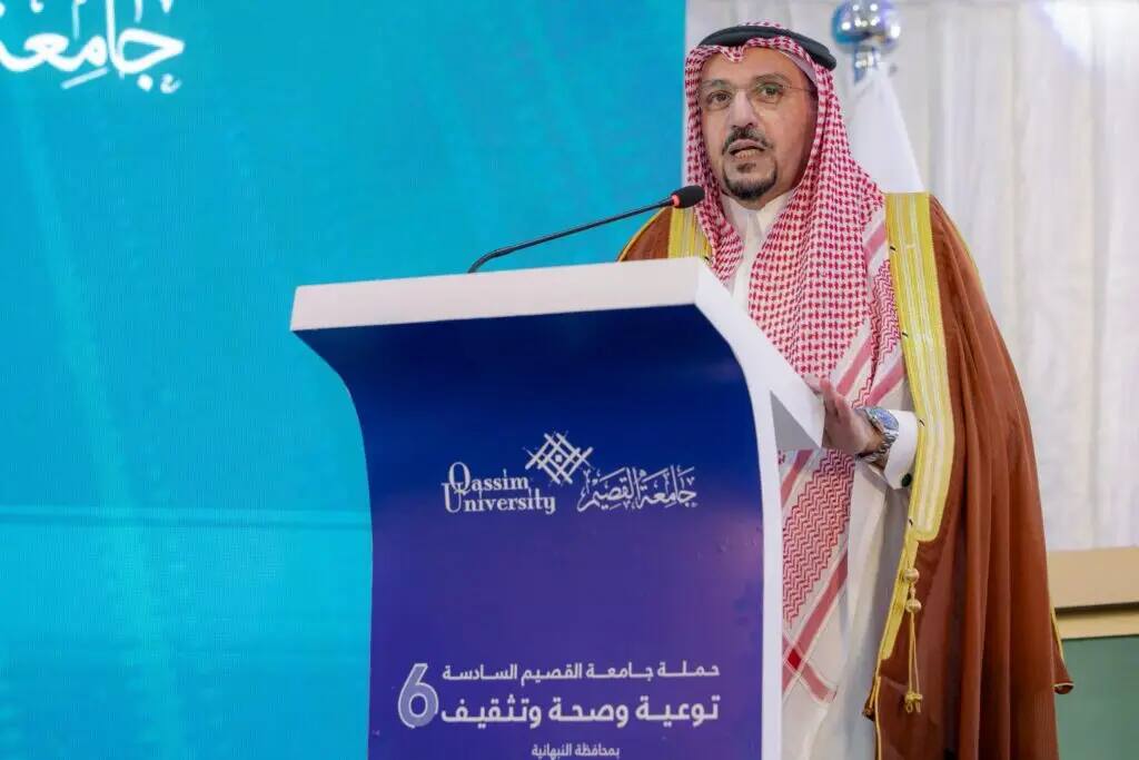 رجل مرتدياً الغترة والعقال والبشتت السعودي الرسمي أمام المنصة التي تحمل شعار جامعة القصيم، ليلقي كلمة خلال فعالية "حملة الجامعة الشاملة". تم تصميمها في شاشة زرقاء تحمل نصوص عربية لتشير إلى مقاطعة النبهانية، وتبرز الإشادة بجهود أمير منطقة القصيم وتكريمه ضمن برنامج رسمي.