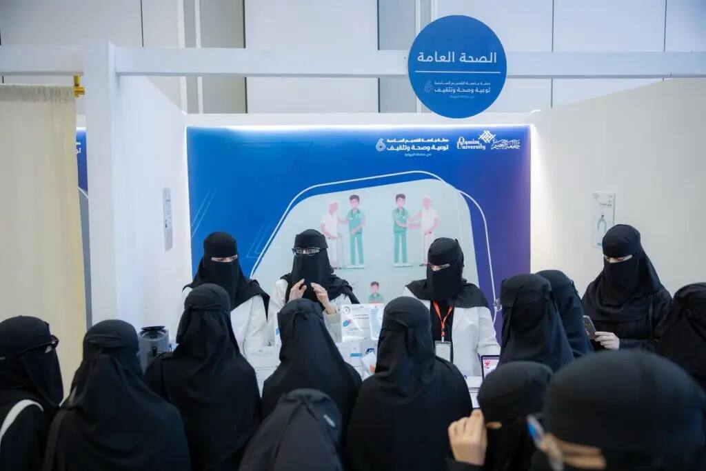 A group of women wearing abayas and dark niqabs gathered around the health awareness hall at an event in Nabhaniyah, where health staff wearing white coats and protective masks provided health education to attendees. Educational posters were also displayed in the background, while some of the men wore the Saudi shemagh, aqal and bisht, the official attire of the event organized by Qassim University.