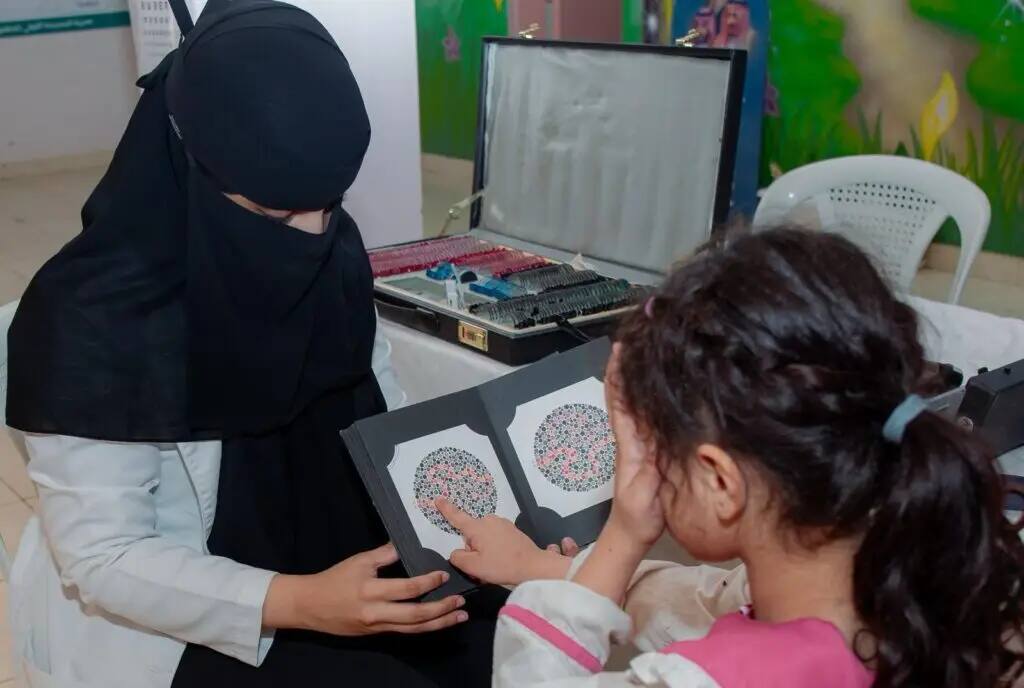 As part of an awareness-raising event to promote awareness of the importance of eye health, a woman from Qassim University stood in front of a child's color screening test in Nabhaniya district. A number of men took part in the weekend in their traditional attire, including the Saudi shemagh, ghattara, headband and bisht. Special tools for vision screening and optometry tests are also nearby, highlighting the interest in the scientific and organizational aspects of this health event.