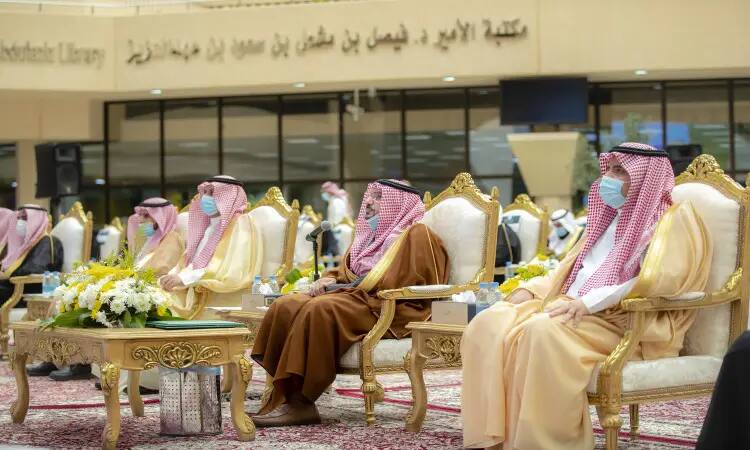 A number of men dressed in ghutra or shemagh and aqqal, as well as the Saudi bisht, sit on plush chairs during a children's event in Qassim held in a hall decorated with floral interiors and a plush carpet; behind them are books in Arabic pinned to the wall.