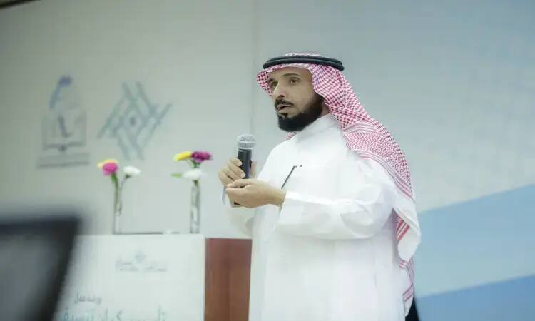 رجل خاطرة سعودية وبشتاً سعودياً، الاتصال خلف منصة الزينة بالزهور ويتحدث عبر الميكروفون في المدرسة، بينما يتتبع بصماته ونصوصه العربية ويتفاعل مع القصيم وشركاء التنمية المحلية.