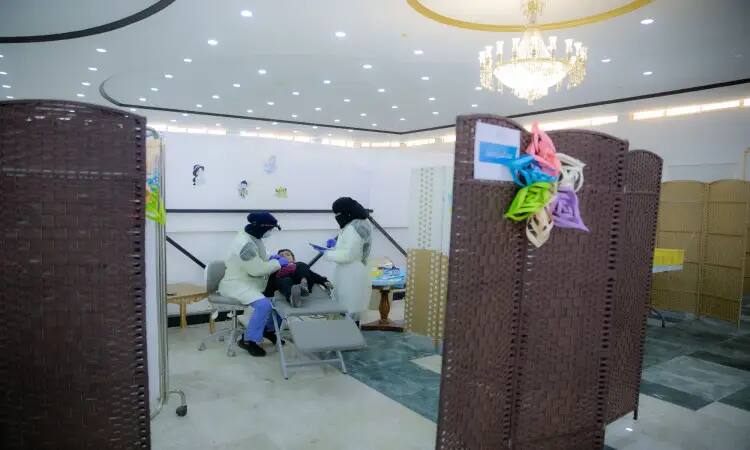 Because two medical staff, dressed in a Saudi Arabian ghutra and bisht, are caring for a patient at the Qubba Center, in a clinic divided by decorative partitions and bright lighting, from which a chandelier hangs. This unique volunteering opportunity showcases the identity of Qassim University and the richness of Saudi heritage details.