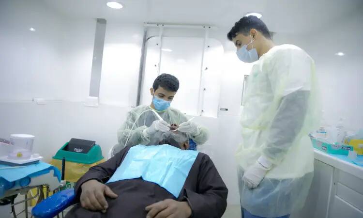 Absolutely! This is your revised official description, tailor-made for the context you mentioned: "Two dentists, dressed in the official Saudi Ghutra, Eqal and Bisht, Namsa Shemagh and Eqal, are treating a patient lying on a dental chair inside one of the rooms of the illuminated dental caravan clinic at the Emirates Dome Center of Qassim University.