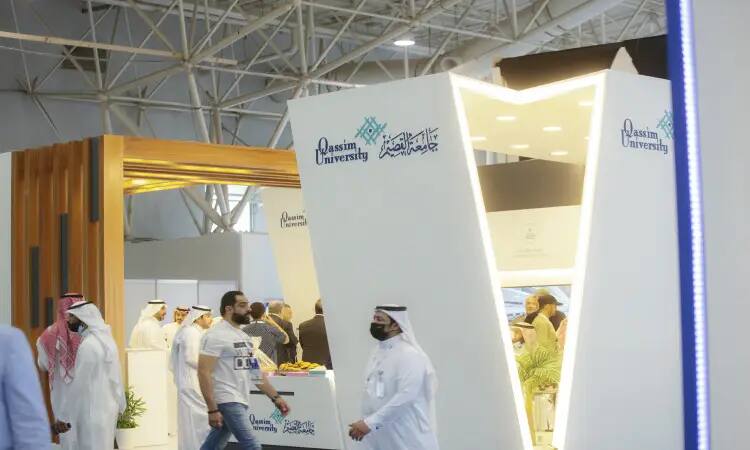 Visitors walk around Qassim University's modern pavilion at the Middle East Poultry Exhibition in Riyadh. It is characterized by flexible designs bearing the university's logo and texts in Arabic. A number of visitors and speakers are seen wearing the Saudi Shemagh or Saudi Ghutra with a headband, in addition to a Saudi video performance, in a scene that reflects the authenticity of the national identity and the university's distinguished academic mission.