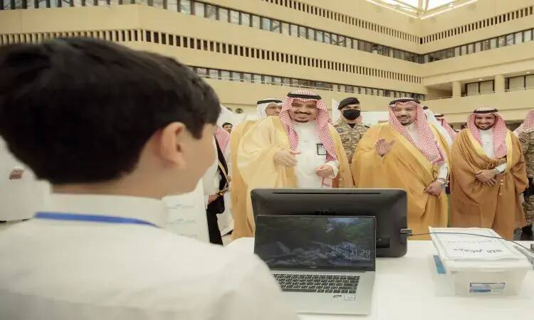 مجموعة من الرجال السعوديين الحاضرين الغترة أو الشماغ والعقال والبشت السعودي، يبتسمون ويتفاعلون مع طفل أمام شاشة عرض جهاز حاسوب وأوراق داخل مبنى حديث، وذلك من خلال فعاليات معرض المبدعين في جامعة القصيم.