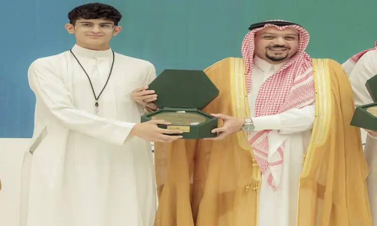 يتسلّم شاب يرتدي ثوبًا أبيضًا خلال معرض مبتكر 2022 من رجل يبتسم، مرتديًا الشماغ السعودي، والعقال، وبشت السعودي التقليدي؛ حيث لم تعد لوحة شرفية خضراء على احتفاءً بالطلبة المبتكرة من جامعة القصيم.