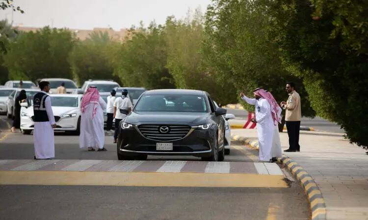يشرف مجموعة من الرجال مرتدين الغترة السعودية، الشماغ، العقال والبشتاء السعودي على حركة السيارات – ومن ثم فإن المركبات مازدا تنظيم من نوع أسود SUV – في شارع تصطف على جانبيه بالقرب من الجامعة من خلال مؤتمرات حزب التحرير. ويتواجد عدد من المركبات المنتظرة في طابور الدخول، إلى جانب طالبات مرور الدفعة 19 بين أروقة المشاة القريبة.
