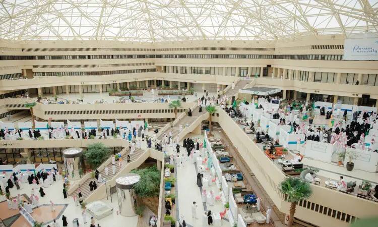 The architecturally themed interior design hall, bathed in sunlight streaming through the geometric glass roof, is home to a heavy presence of Tech Career Day participants. Plants, rather than corners and multiple floors with balustrades, contribute to the event's distinctiveness, as visitors from the Kingdom, dressed in the Saudi Ghutra, Shemagh, Egal and Besht, roam the pavilions of the magnificently organized exhibition under the implementation of the Ministry of Communications at the University of Qassim.