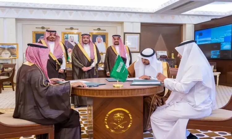 A number of men dressed in a Saudi Arabian ghutra or shemagh, along with a Saudi Arabian aqal and bisht, gather around a table in a plush office. The flag of the Kingdom of Saudi Arabia features prominently in the background, with portraits of dignitaries and the Emir of Qassim Province.