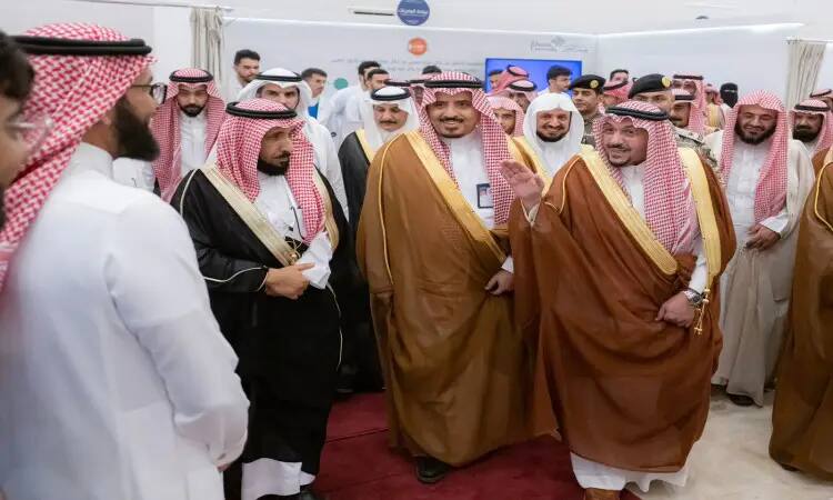 A group of Saudi men, famous for the Saudi dress with the shemagh or Saudi ghutra and headband, gather at an event held inside the Qubba Center hall. In the middle of the audience are a number of participants celebrating the Saudi bisht decorated with a golden ball, exchanging greetings and smiles on the occasion of the fourth university campaign celebration, in the presence of His Highness the Emir of Qassim.