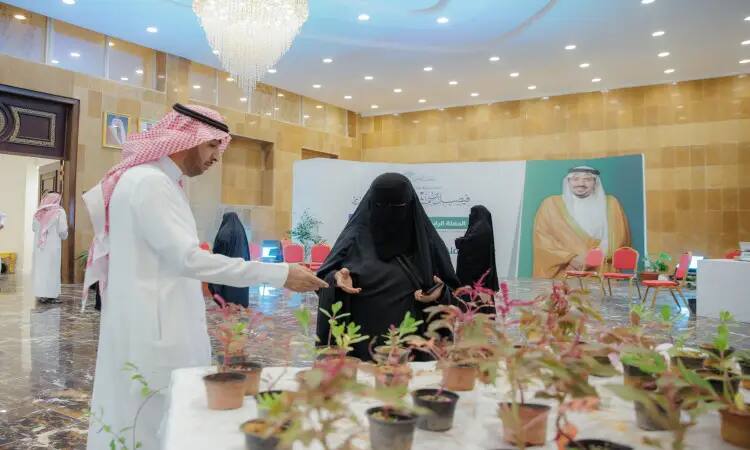 رجل يحتوي على يرتدي الغترة والعقال والبشت السعودي إلى جانب ترتدي الشماغ السعودي، بجانب طاولة على مزروعة خضراء في أصص، وذلك من خلال فعالية توعوية صحية وتثقيفية نظمت لمنسوبي تؤكد ات الجامعة. تسجيل في الخلفية عدد من وكراسٍ فارغة مع لوحة كبيرة تحمل صورة رجل بارز، وذلك في قبة المركز عند القصيم.