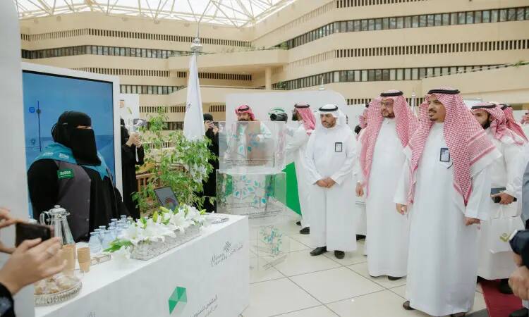 مجموعة ميامي من الرجال بزيٍ سعودي تقليدي تشمل الغترة أو لباس الشماغ، والعقال، والبشت السعودي، إلى جانب سيدة ترتدي سترة مع صدري أسود الفيروزي، في منصة مخصصة داخل المعرض يقام بمناسبة "الملتقى الخامس لأندية نزاهة" في الجامعة. ويحيط بالمنصة العشبية وزجاجات ومواد تعريفية بالمعرض.