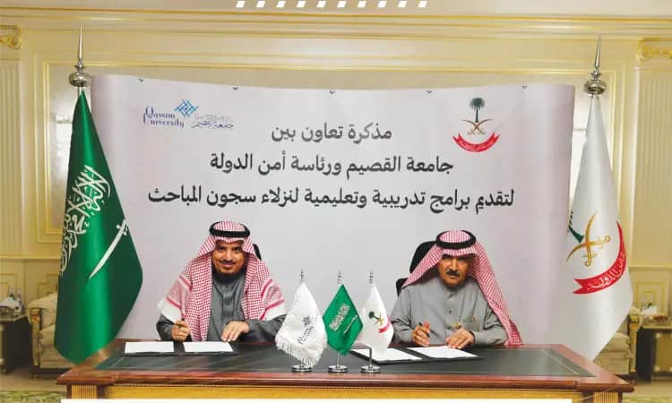 يرتدي رجلان يرتديان البشتت السعودي والغترة والعقال على طاولة تتوسطها مستندات عادي، ويحيط بهما علم المملكة العربية السعودية ويعلم الوطنية. وخلفيتهما غير مرئية باللغة العربية للتوقيع على التوقيع التعاوني بين جامعة القصيم ورئاسة أمن الدولة.