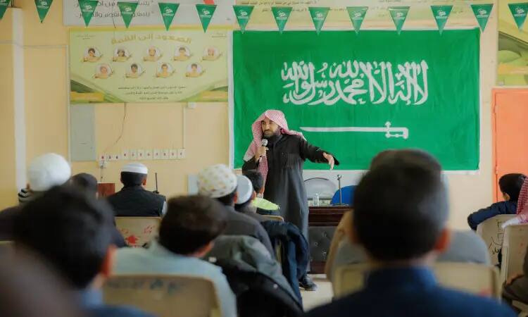 Dressed in a Saudi ghutra and headband, and wearing a traditional Saudi shawl, a retired center liaison man addressed the audience in a hall decorated with green banners and topped with the flag of the Kingdom of Saudi Arabia. The man held an awareness session on health, while a number of listeners followed his talk with great interest.