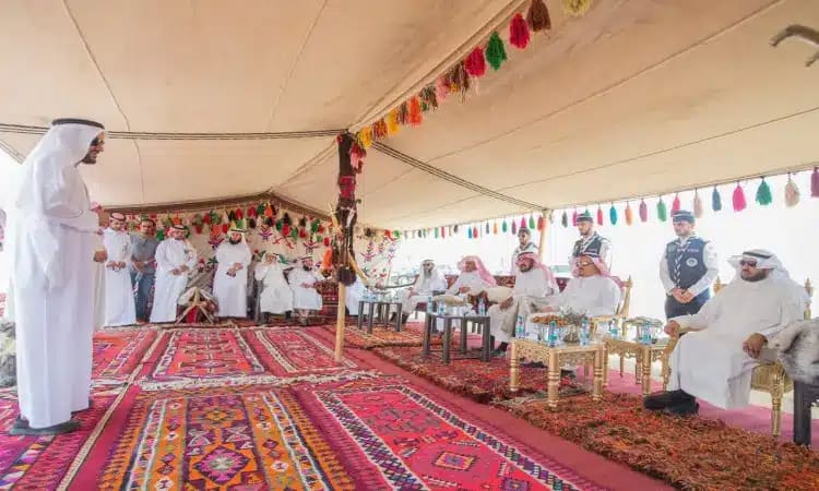 يجتمع عدد من رجال مرتدين الغترة أو الشماغ السعودي مع العقال والبشت السعودي، ويجلسون ويقفون تحت خيمة مزينة بالسجاد الملون والشراب، وتوزع على طاولات المشروبات المتنوعة. ولهذا الاجتماع الرسمي ضمن فعالية نظمها جامعة القصيم بمناسبة زراعة 1800 شجرة خلال أسبوع الشجرة.