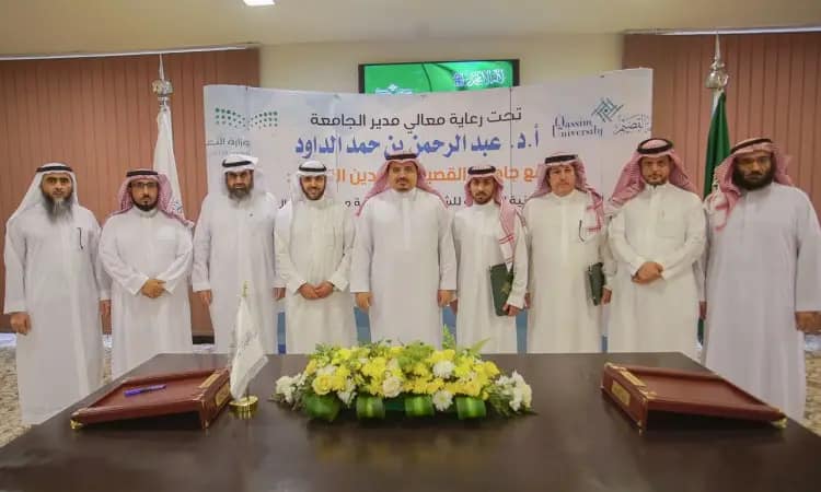 A group of men wearing the Saudi ghutra or shemagh with the Saudi aqqal and bisht, a front for the water plant project of Qassim University. He tells me two tables with documents and flower arrangements on them.
