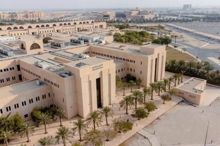 صورة جوية لمبنى جامعي حديثي الولادة وواسعة باللون البيج، وتضم كلية العلوم التطبيقية في القصيم. يحيط بالمبنى عدد من عدد النخيل، والاستعانة بأرقام السيارات وعدد من المباني الإضافية تحت أي شيء.