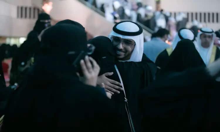 رجل للاتصال بزيٍ سعودي تقليديّ يرتدي غترةً سعودية، عقالاً وبشتاً أنيقاً ويبتسم وهو يعانق إحدى اللجان، التي قد تكون من أمهات الخريجين، وذلك وسط جمع من الحضور في ثقة تخريج الدفعة داخل قاعة الجامعة. وأشار بعض المشاركين إلى أنهم يخصصون تخصيص أصواتهم ويتبادلون الأحاديث في ما يسودها الفخر والسرور بمناسبة هذا الإنجاز الأكاديمي في جامعة القصيم.