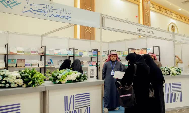 A number of people dressed in ghutra or shemagh and aqqal, as well as the Saudi bisht, gather around the Qassim University pavilion at the Qassim Book Fair. They are there to show off their differences and debate among the members of the Labor Party, who are decorated with flowers, books and banners with Arabic texts and university publications.
