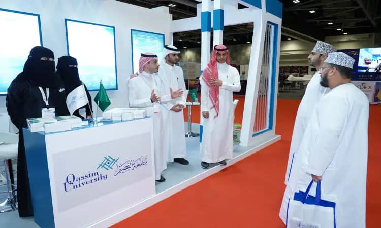 عدد كبير من الأشخاص مرتدين الغترة والعقال والبشتاء السعودي أمام جناح جامعة القصيم خلال المعرض العالمي للتعليم العالي. كان مرور الوقت بحقائب بينما توقف العدالة بجوار منصة العرض التي تزيّنت بمنشورات تعريفية، وعلمت المملكة العربية السعودية، ومواد تعريفية خاصة بفعاليات.