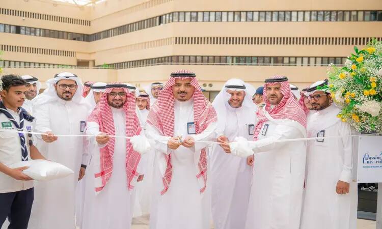 A group of men in their Saudi uniforms, wearing the Ghutrah or Shemagh with Eqal, and wearing Saudi pashmina, lined up to cut the ribbon to mark the opening of an important awareness-raising event. The coordinators held the scissors as they stood with their official presence, in an outdoor square with the Zahraa Jamil coordination in the middle and the university buildings next to it, embodying the grandeur of Qassim University in organizing such meaningful events.
