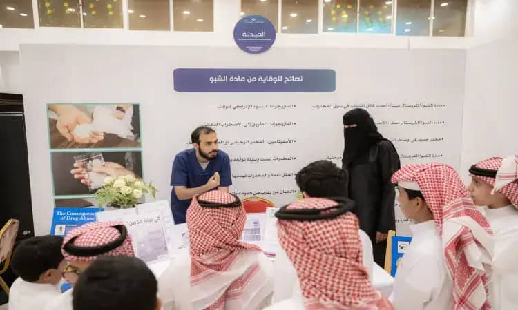 رجل يقف بشت سعودي وشماغاً مع عقال، وسيسيدة يغترة سعودية قديمة، يقدم التثقيف لطلاب في ركن تعليمي حول التعرف على المخدرات والتعاطي، وذلك ضمن فعاليات جامعة القصيم. كما يمكن اختيار قائمة الطعام ولون الخلفية الركن محتوى توعوية ومنشورات ثقافية تحمل رسائل عن الصحة والتوعية.