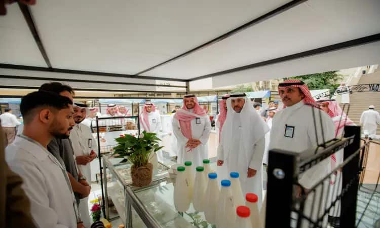 الاتصال مجموعة من الرجال مرتدين الغترة السعودية أو الشماغ مع العقال والبشت السعودي، إلى جانب عدد من المختصرين تمسك المؤثرين الخبرية، حول منصة الاتصال التعاونية الحليب ونبتة مزروعة في أسيست، وذلك عرض ضمن معرض داخلي أُقيم بمناسبة يوم الأطعمة في جامعة القصيم، لإبراز فوائد الأغذية العضوية.
