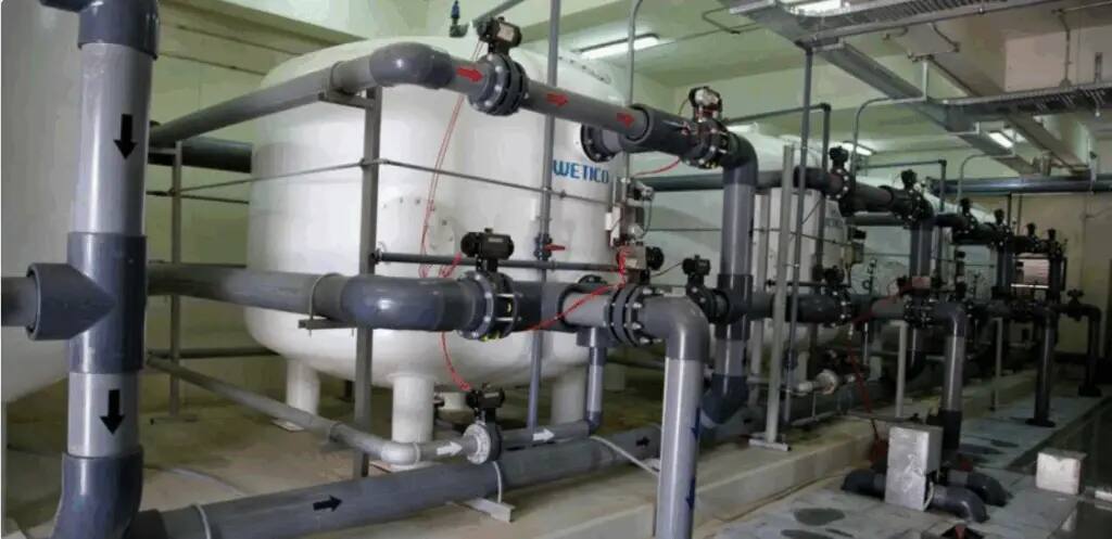 The photo shows the interior of the water facility, where a large cylinder and a vertical network of pipes, filters, and gauges are used for filtration and treatment, in support of Goal 6 initiatives.