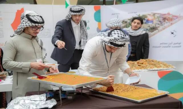 يقوم عدد من الرجال الذين تأخروا الشماغ السعودي أو الغترة السعودية بتقديم وتشكيل صوانٍ كبير من الأطباق المتنوعة ذات الألوان الزاهية من خلال الفعالية الثقافية، وذلك وذلك في ظل وجود ملصقات تعريفية وتقارير حول الهدف الرابع في الخلفية.
