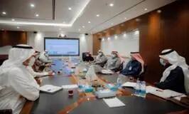 A number of men wearing the Saudi shemagh or Saudi ghatra gather in a dedicated hall in Qassim, sitting around a conference table and discussing a resolution projected on a large screen. Some attendees are wearing medical masks to adhere to specific procedures, and the discussions revolve around Goal 13-related themes.