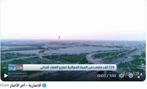 An aerial view of the main road in the big city shows green spaces and buildings, with voluntary text in Arabic at the bottom.