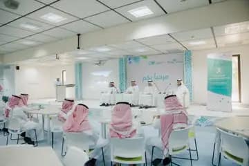 يجتمع عدد من الرجال مرتدين الشماغ أو الغترة السعودية حول الطاولات وعلى المنصة في قاعة المؤتمرات الحديثة، وذلك ضمن فعالية المجتمع أو حلقة نقاش مخصصة لموضوع تقرير الهدف الثاني عشر. ينصح بالملصقات والخلفيات والنصوص والشعارات باللغة العربية.