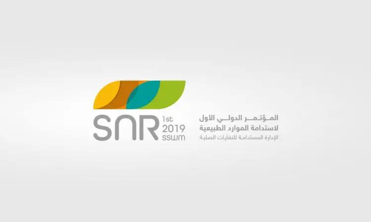 شعار المؤتمر الدولي الأول لاستدامة الموارد الطبيعية 2019 (SNR)، يتضمن أوراق نباتية مجردة، والهدف الثاني عشر، مع نص ثنائي اللغة باللغتين العربية والإنجليزية على خلفية رمادية فاتحة.